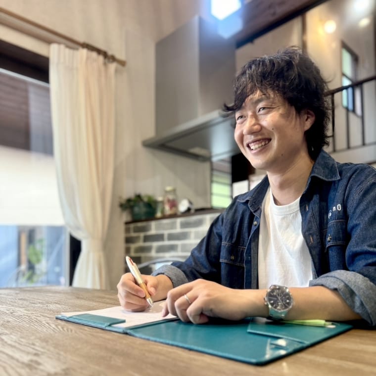 浦川卓也さんが笑顔で書き物をしている様子